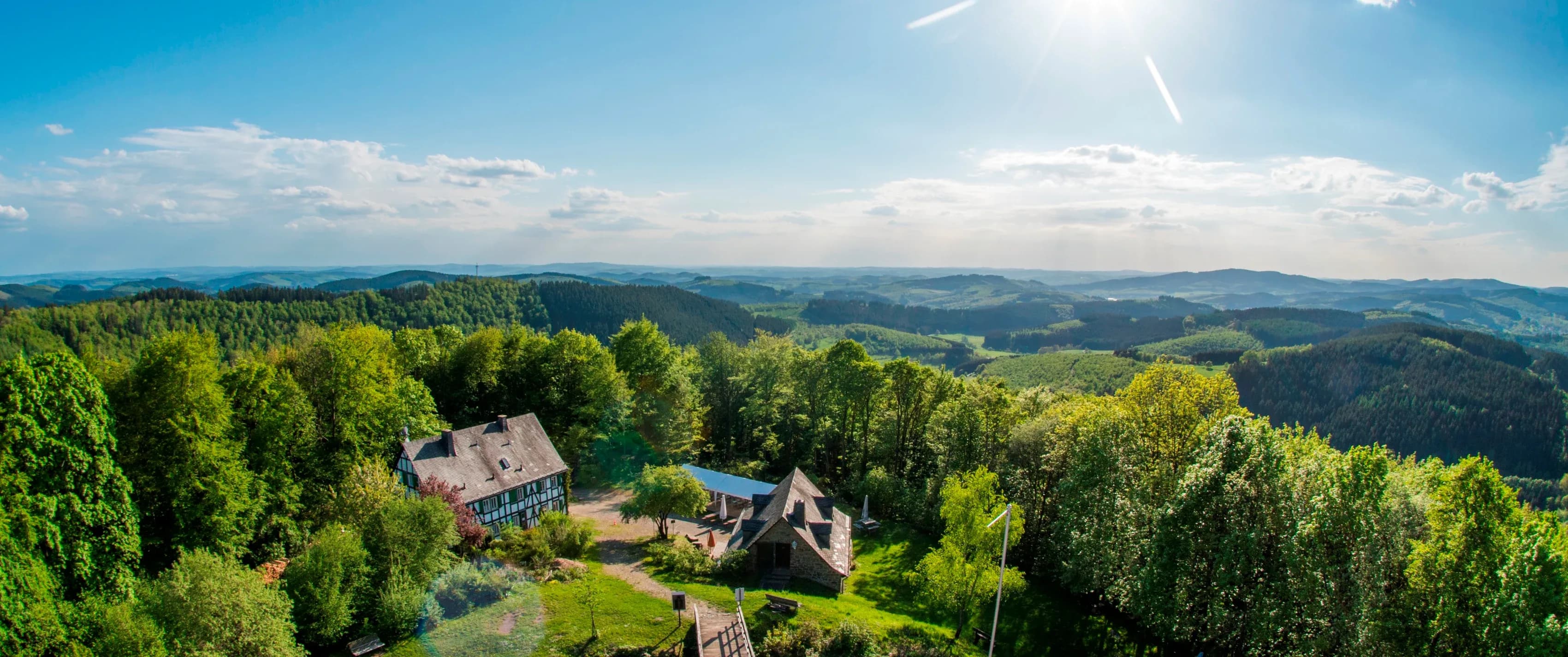 Luftbild einer Mittelgebirgslandschaft mit Wiesen, Wald und einem Fachwerkhof im Tal