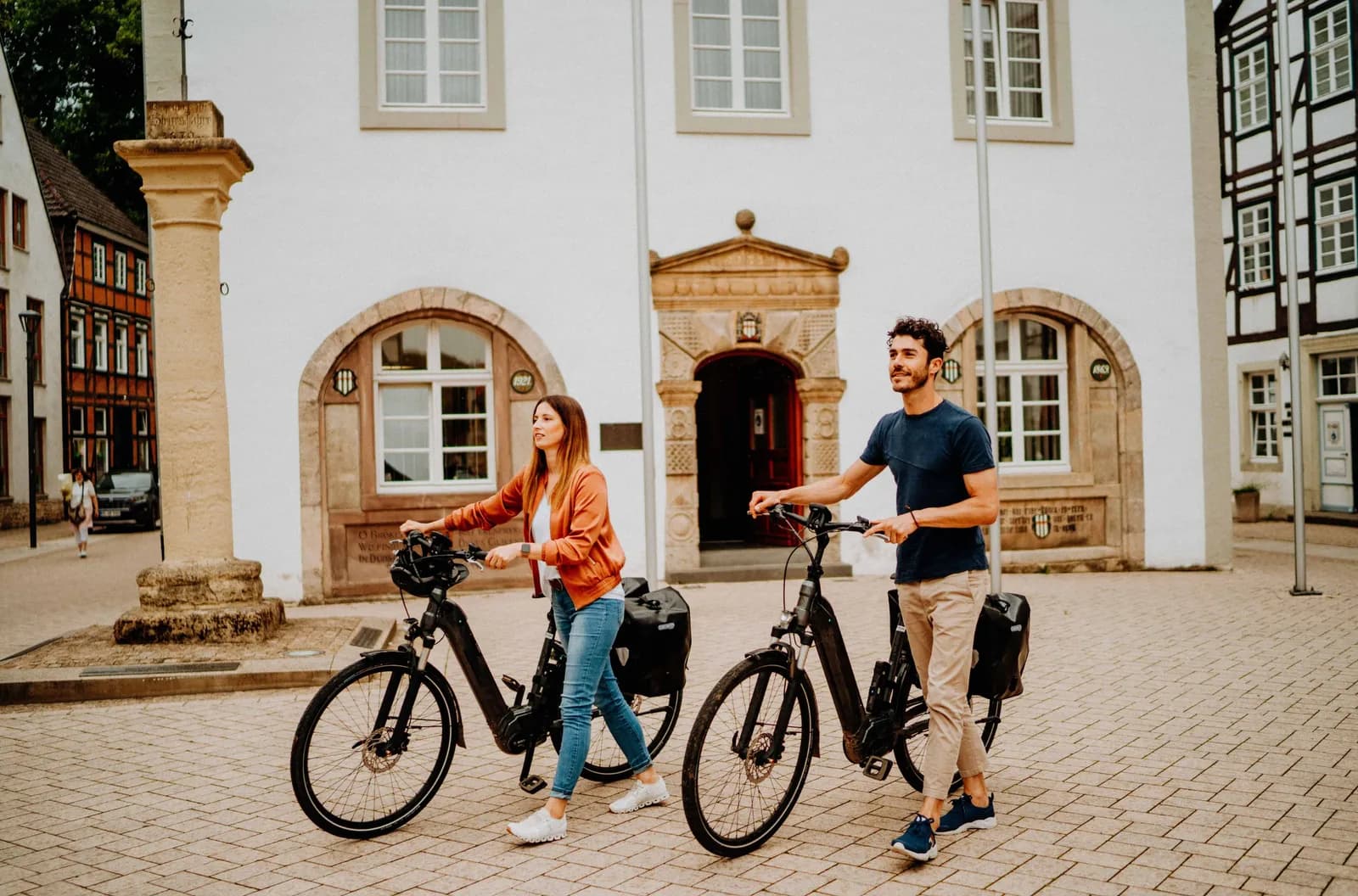 Zwei Personen mit E-Bikes halten am Rand eines begrünten Platzes