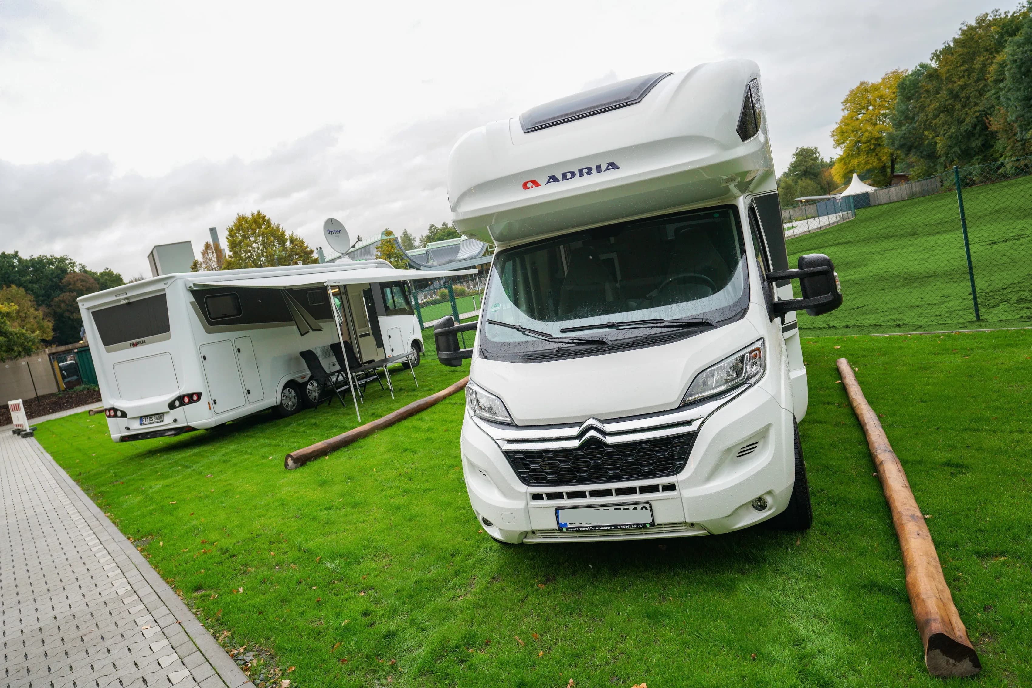 Zwei Wohnmobile auf markierten Stellplätzen neben einer Grünfläche