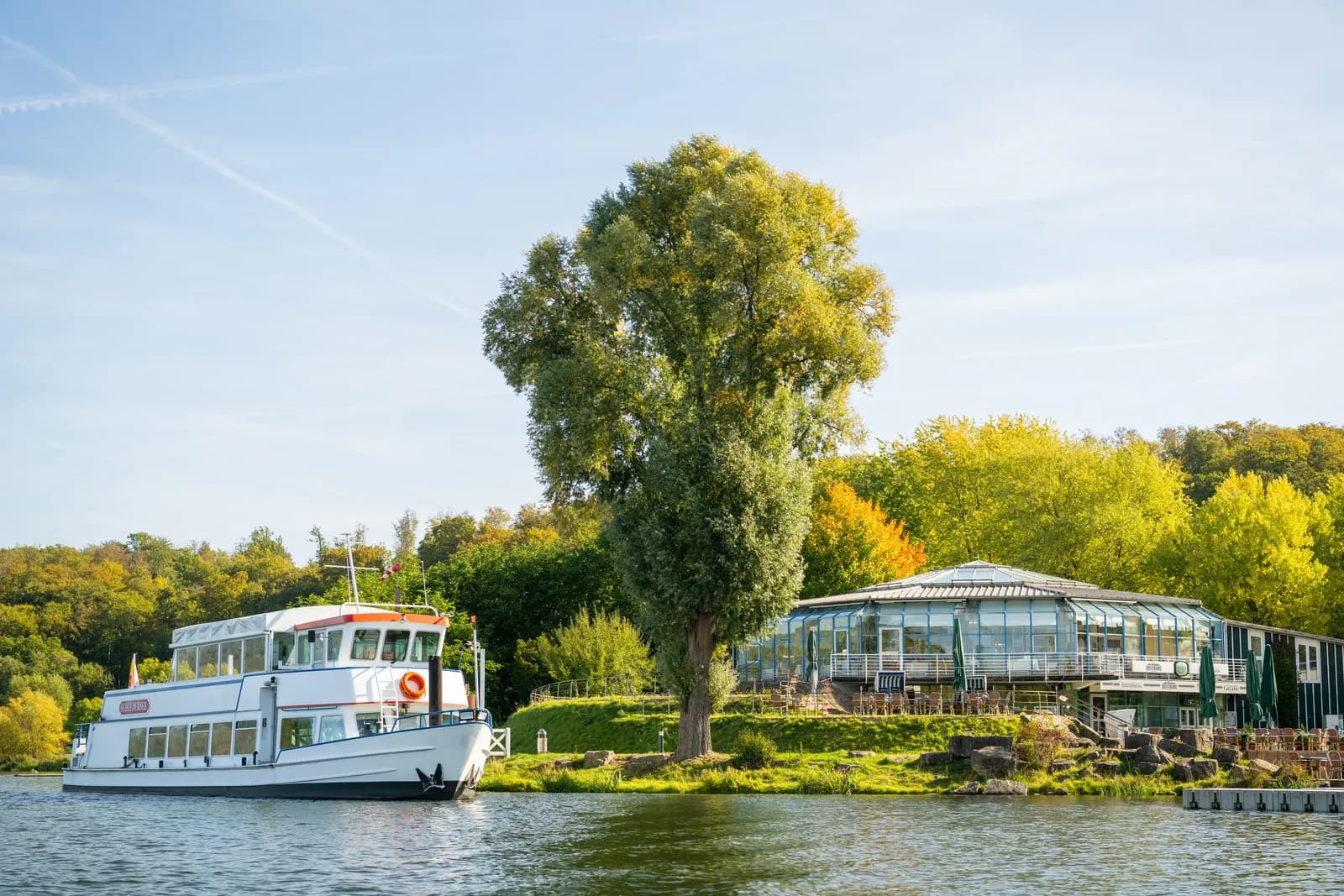 Weißes Ausflugsschiff auf einem Fluss, umgeben von grünen Bäumen