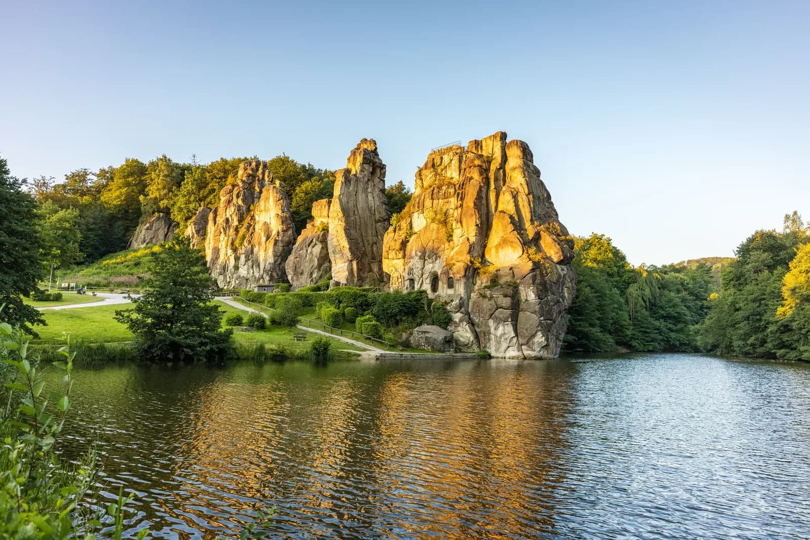 Felsenformation in grüner Landschaft, gespiegelt in einem See bei Sonnenuntergang