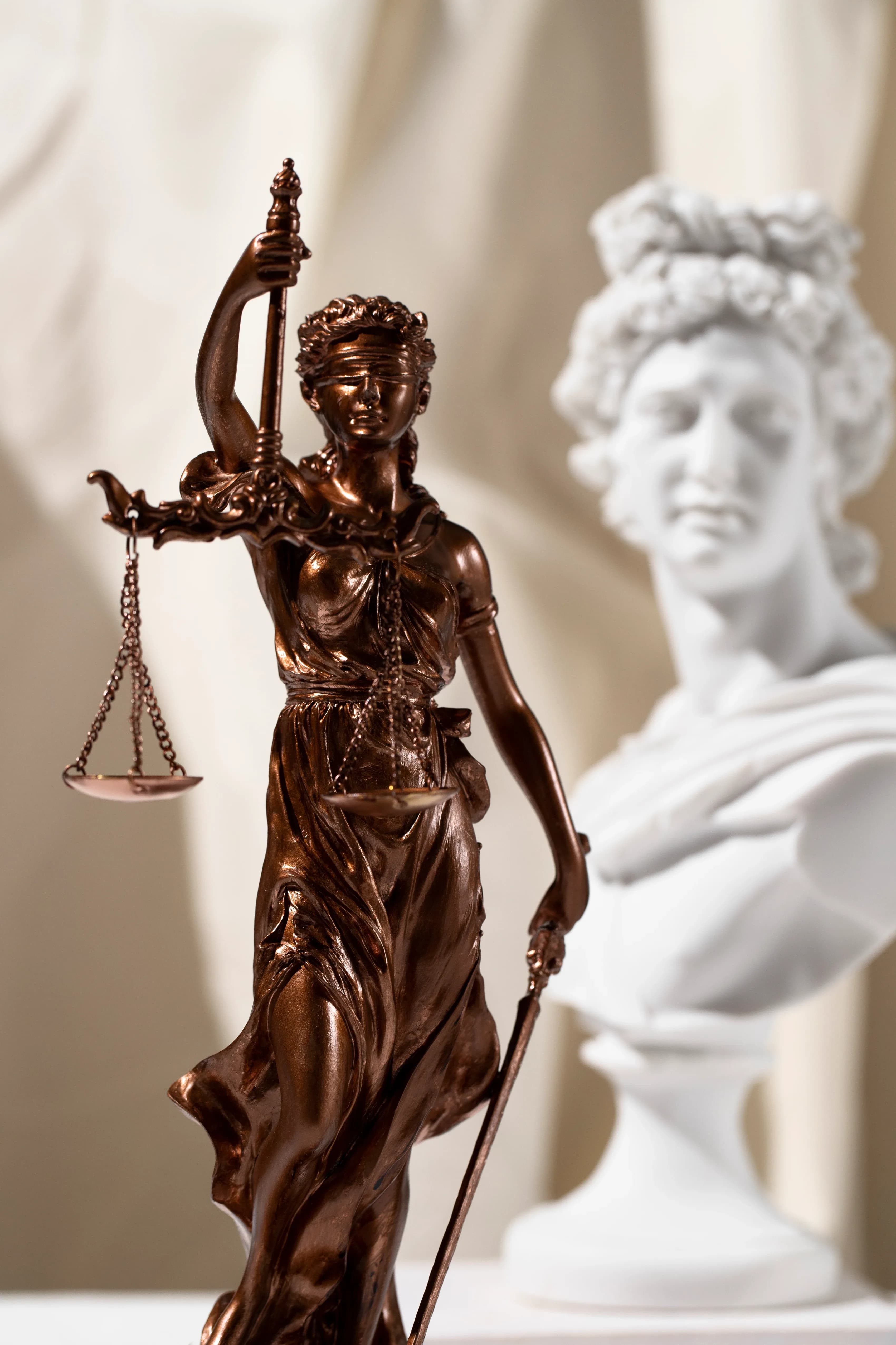 Bronzene Justitia mit erhobener Waage, dahinter ein heller Gipskopf